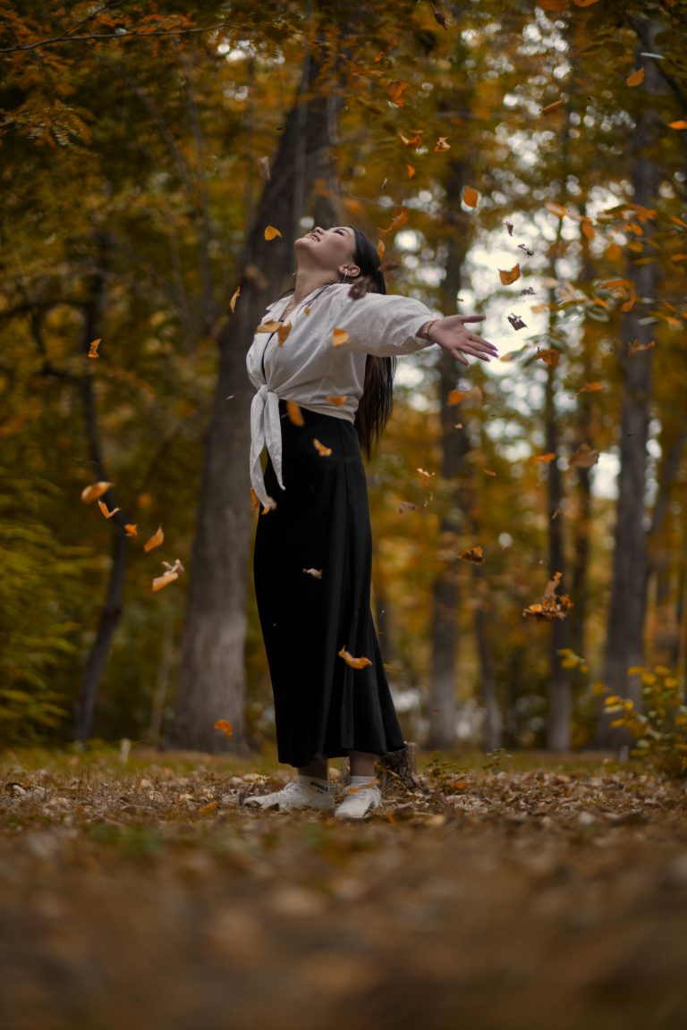 A happy girl is tossing yellow leaves in an autumn park.