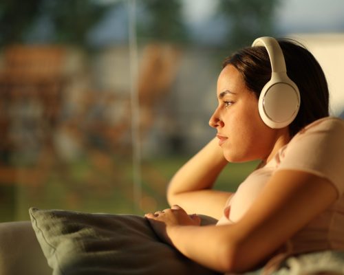 thoughtful woman listening audio with headphone sitting in a couch at home